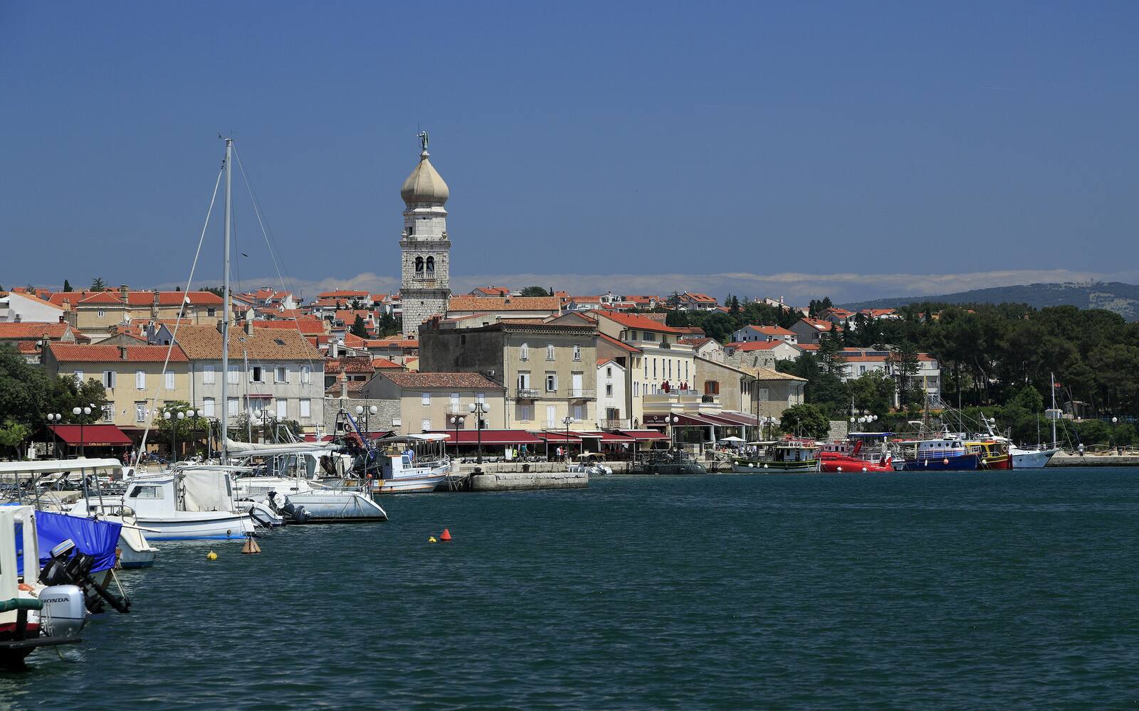 De stad Krk gezien vanaf het water, met boten in de haven en de klokkentoren met uivormige spits boven de huizen