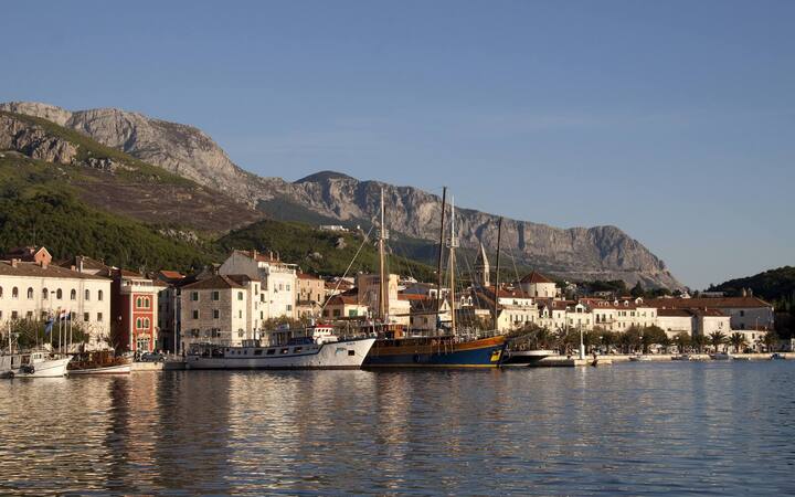 De haven van Makarska met vissersboten en een houten zeilschip, met het Biokovogebergte op de achtergrond