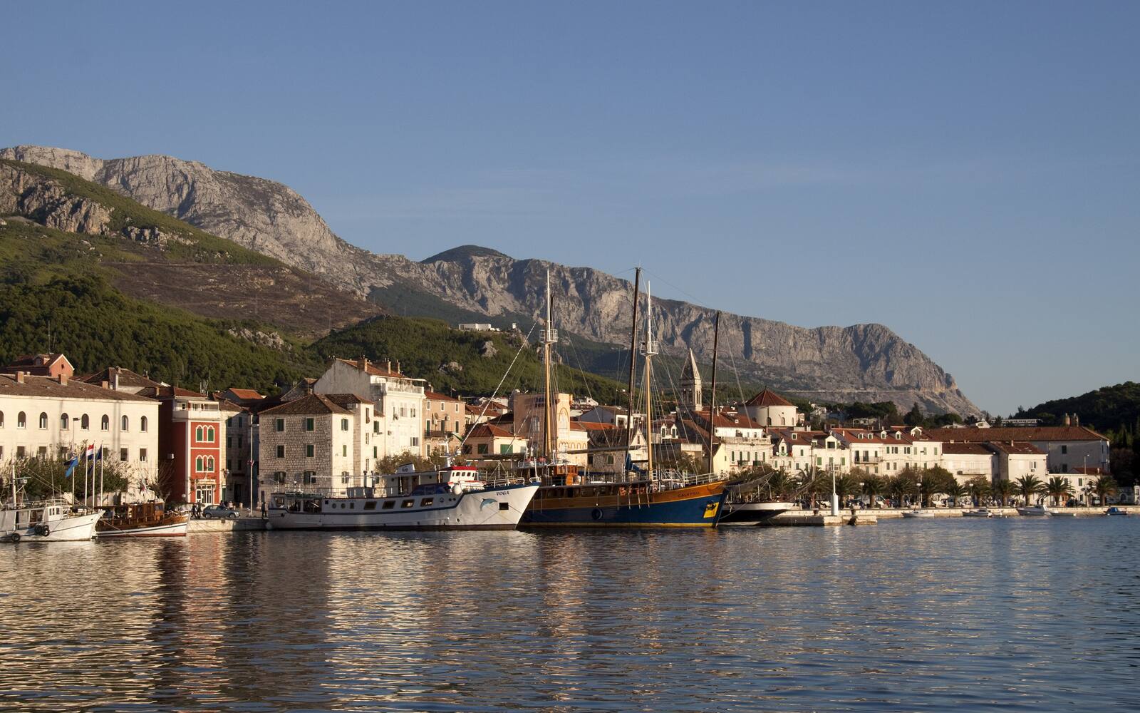 De haven van Makarska met vissersboten en een houten zeilschip, met het Biokovogebergte op de achtergrond