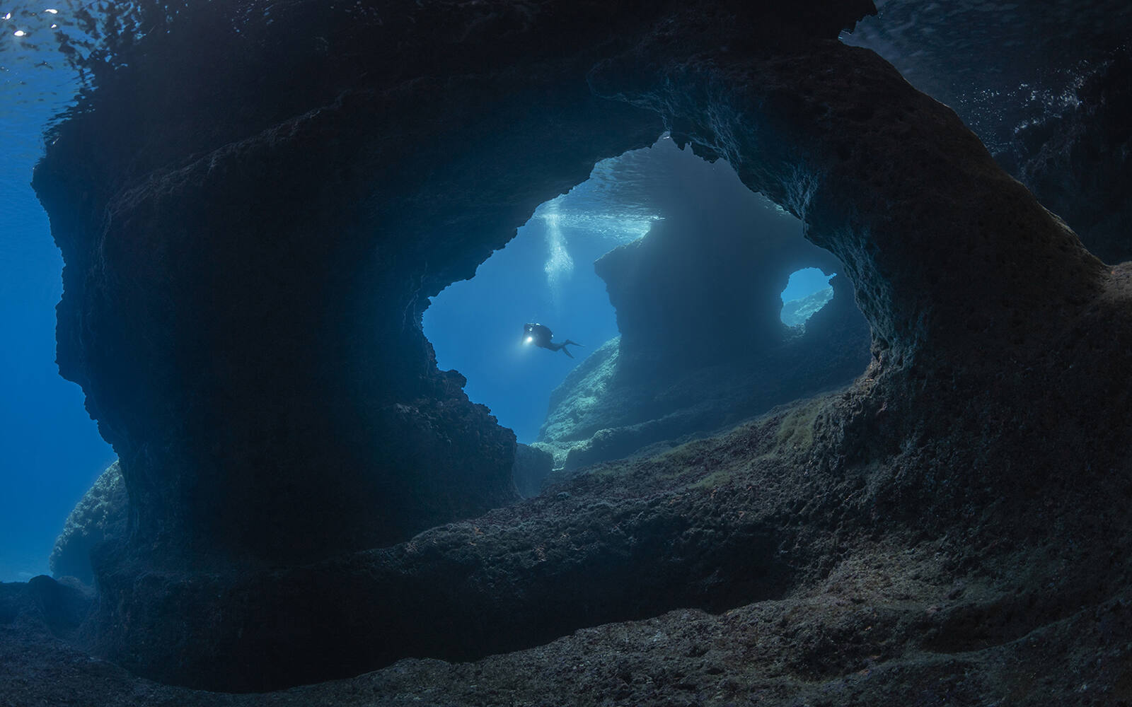 Onderwaterboog in een rots bij het eiland Vis, met een duiker in het blauwe licht