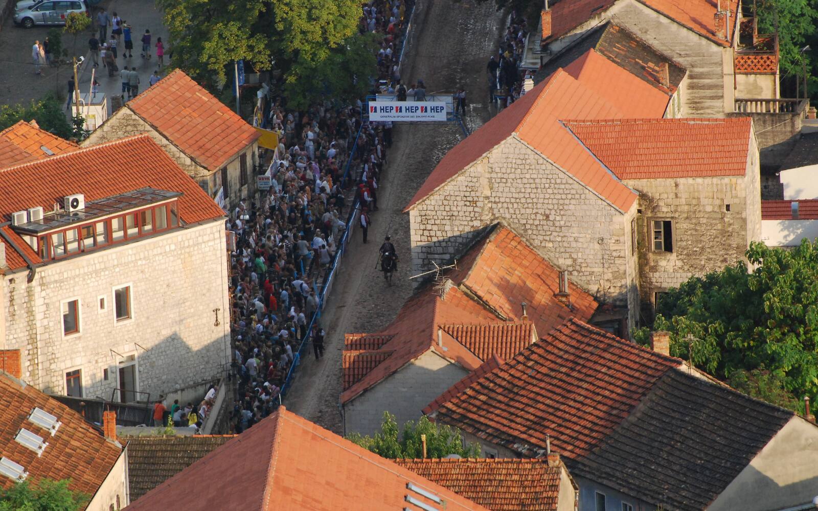 Bovenaanzicht van de Sinjska alka: een volle straat met toeschouwers tussen oude huizen met rode daken in Sinj