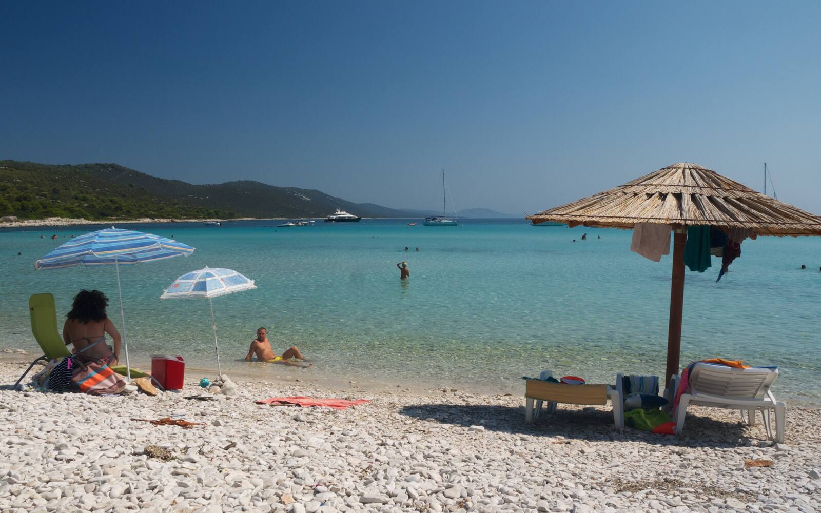 Kiezel- en zandstrand Sakarun op Dugi Otok met parasols, rieten zonnescherm en turquoise water