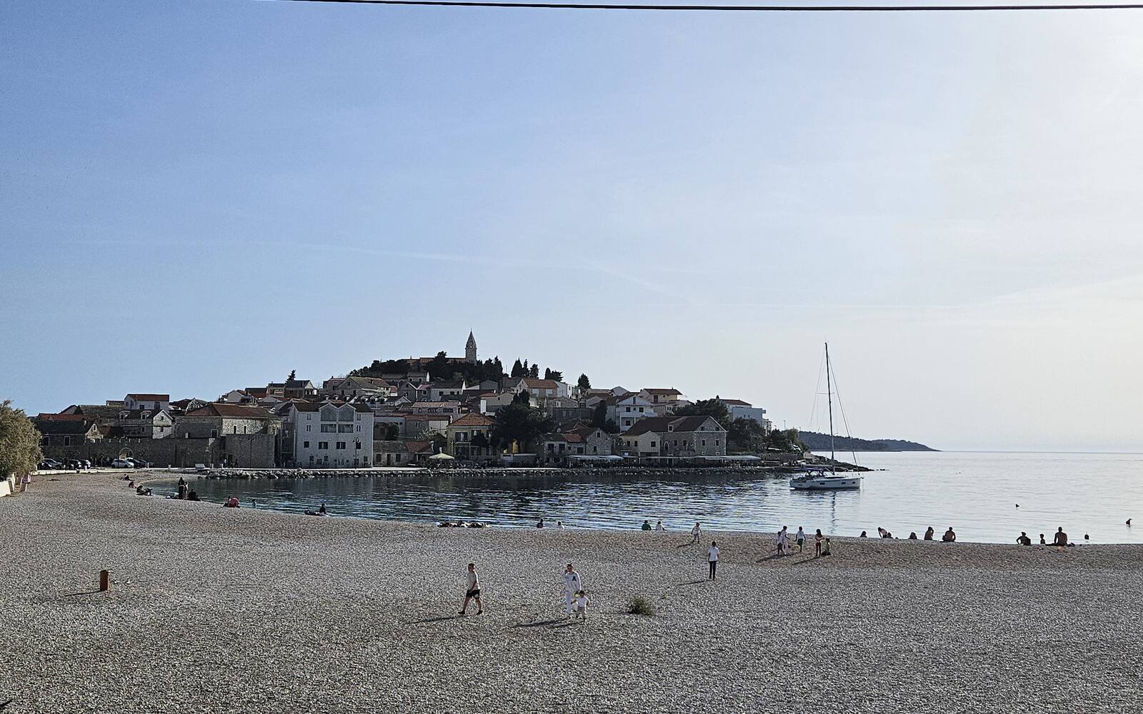 Het oude stadje Primošten op een schiereilandje met de kerktoren op de top, gezien vanaf het kiezelstrand