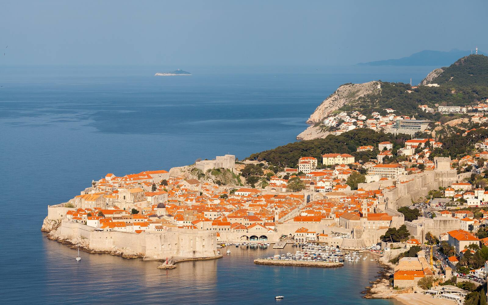 Luchtbeeld van de ommuurde oude stad van Dubrovnik met rode daken en de oude haven aan een blauwe zee
