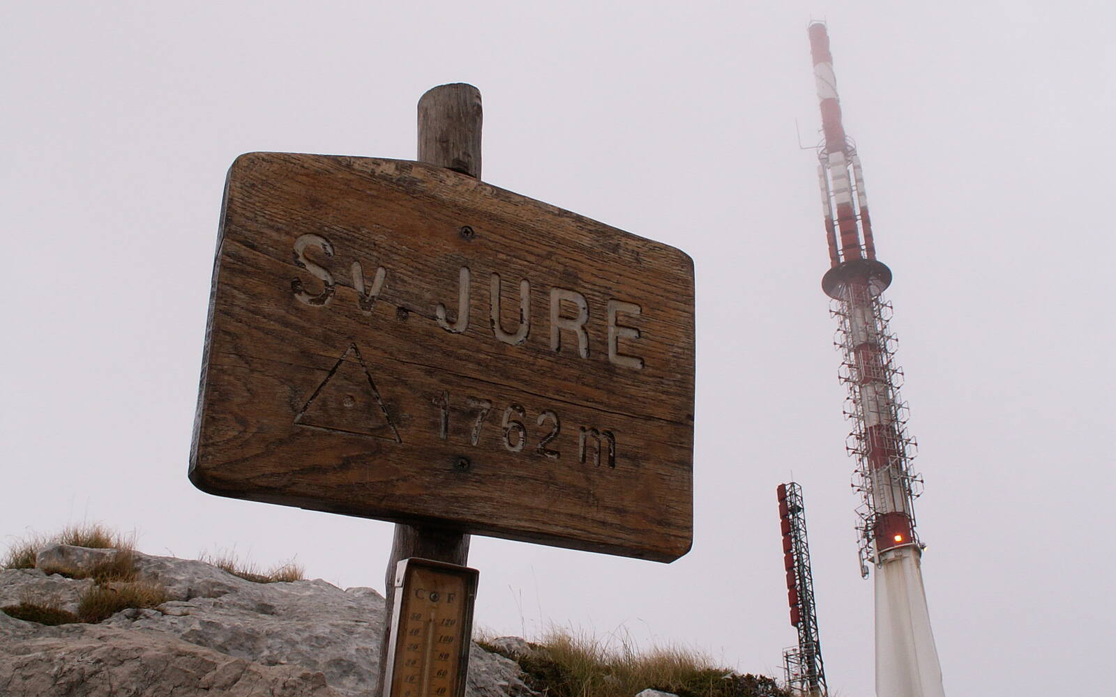 Houten wegwijzer met 'Sv. Jure 1762 m' op de top van Biokovo, met de zendmast in de mist