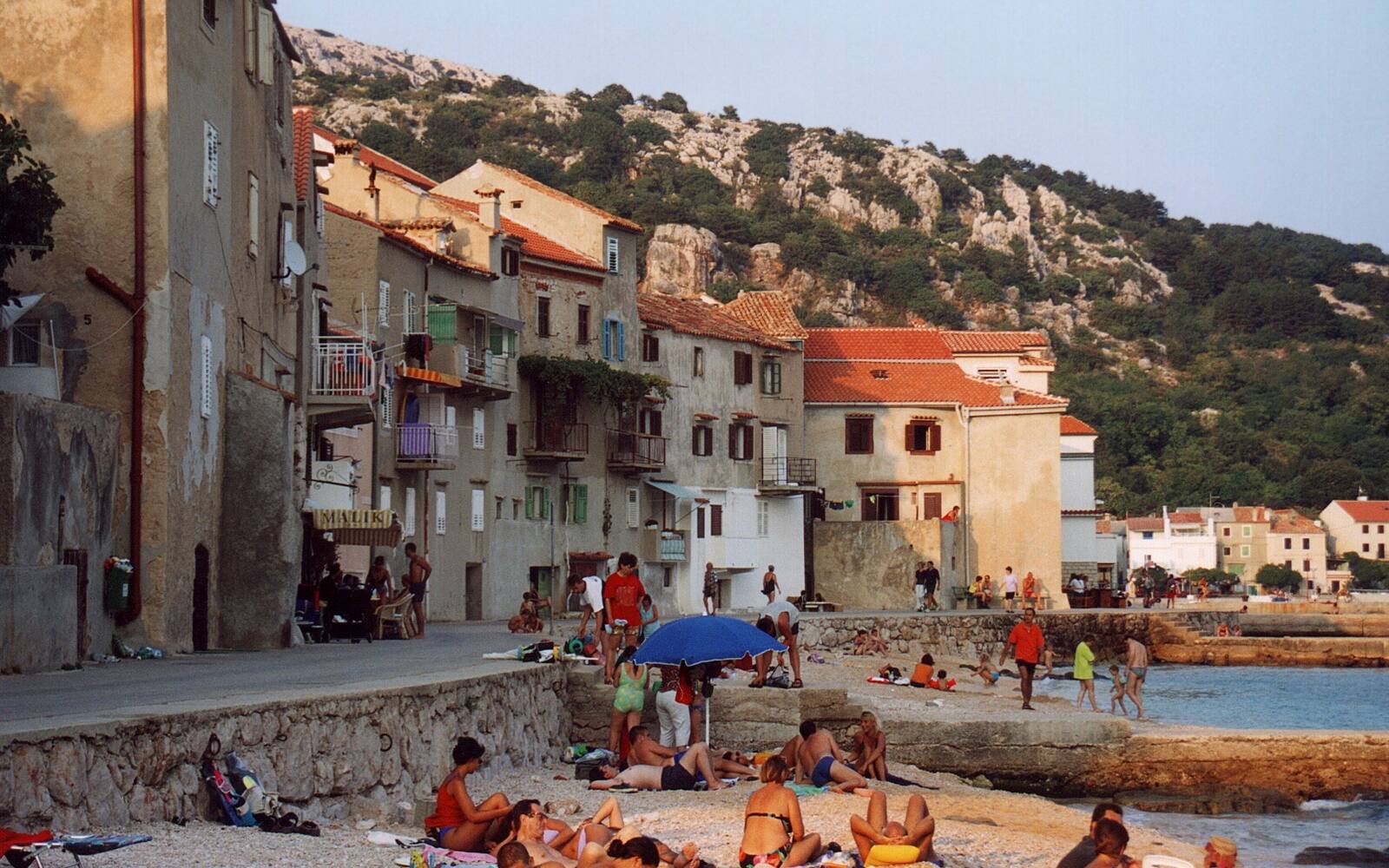 Kustdorp Baška op Krk met badgasten op de kiezels voor oude stenen huizen
