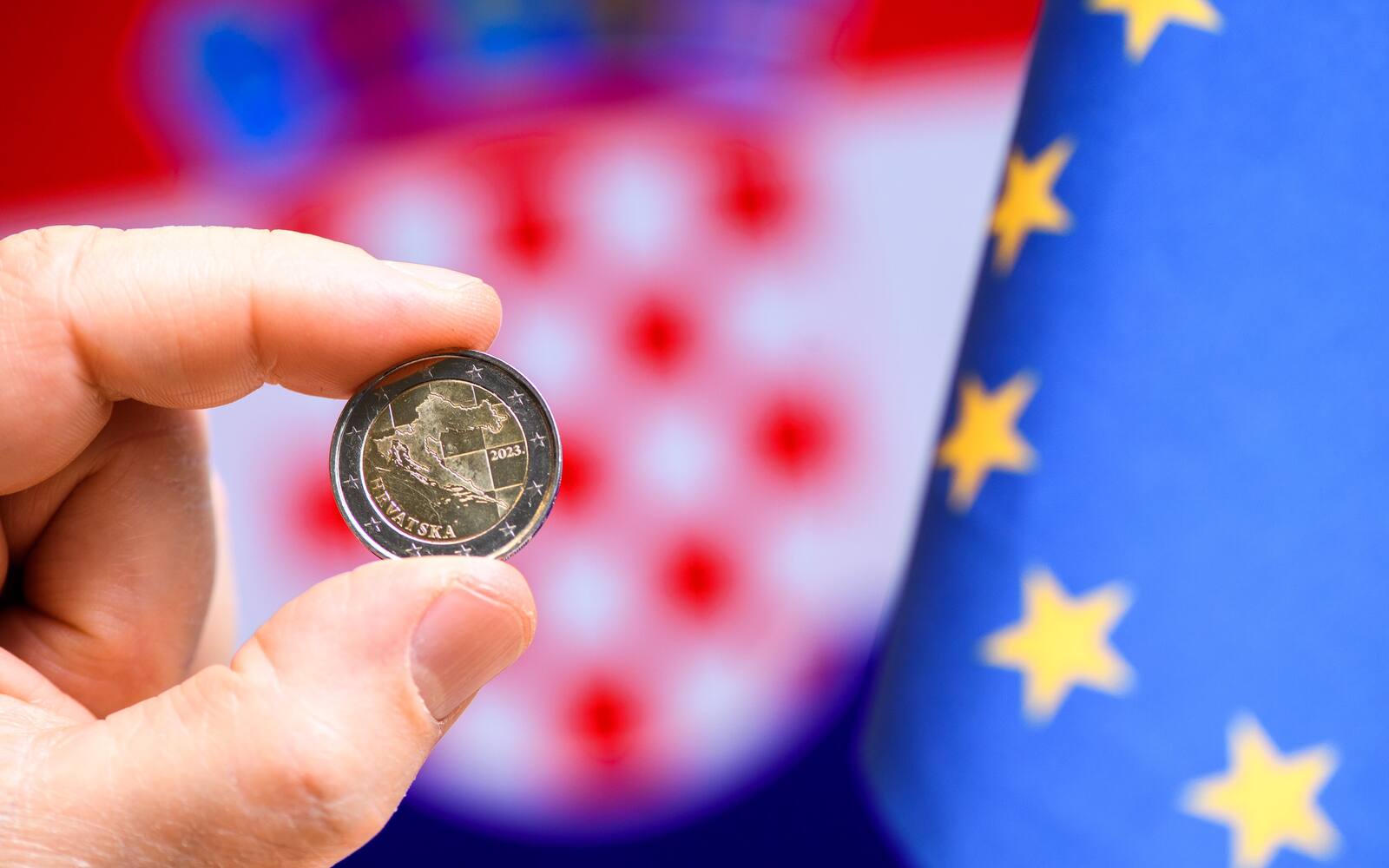 Hand houdt een Kroatische euromunt voor een vlag van Kroatië en de Europese Unie