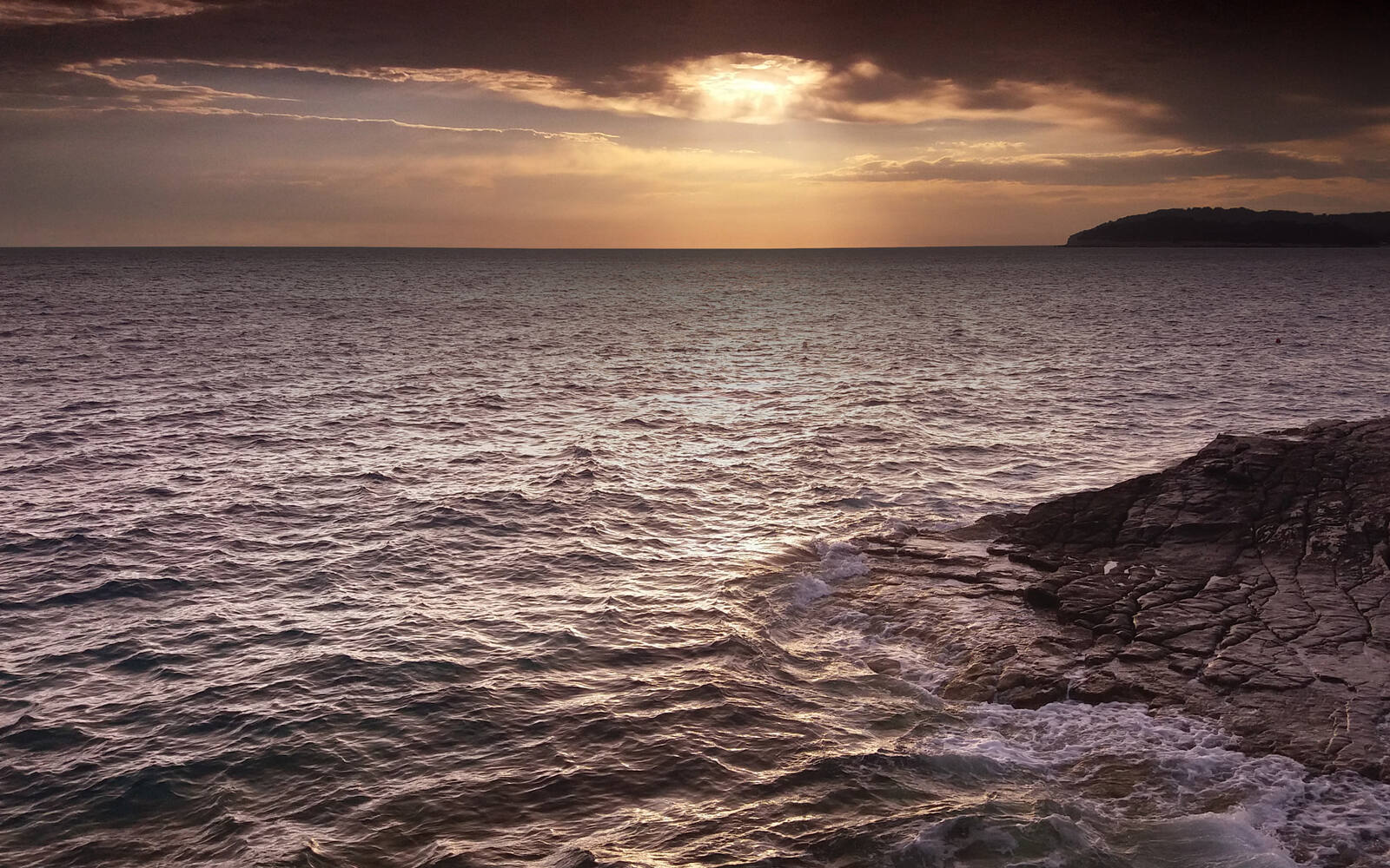 Zonsondergang boven de Adriatische Zee met golven die tegen donkere rotsen slaan