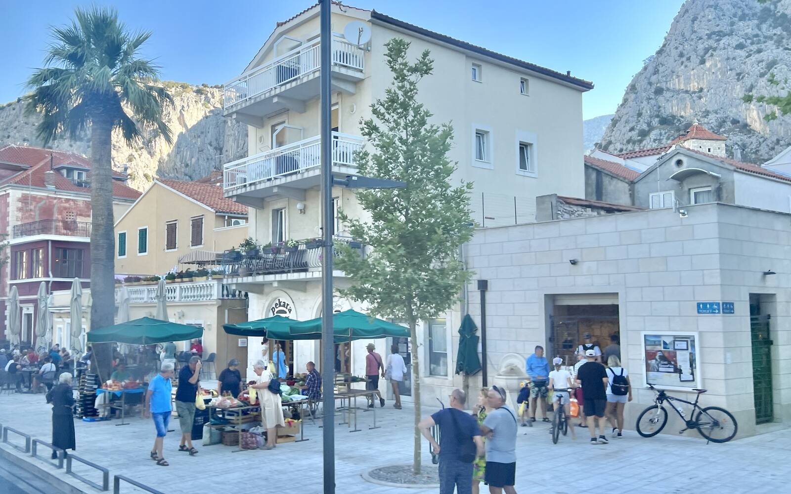 Straat in Omiš met appartementengebouwen, palmen en een terras aan de voet van steile rotswanden