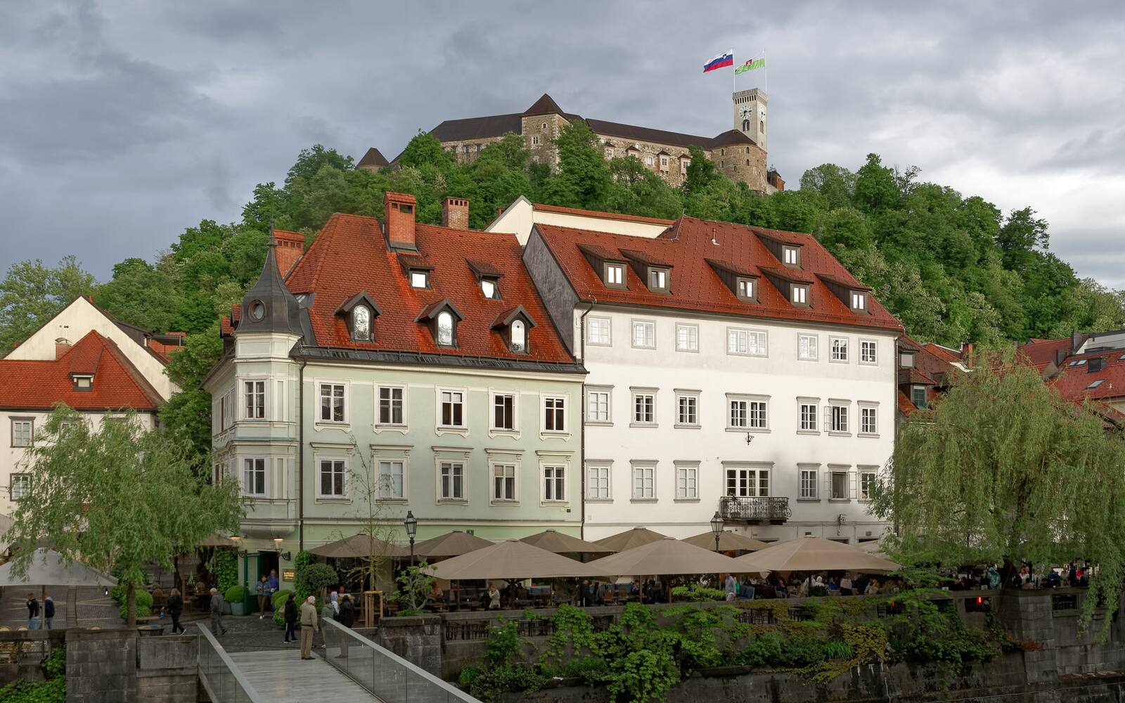 Het kasteel van Ljubljana op de beboste heuvel boven historische panden langs de rivier