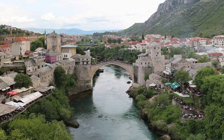 De Oude Brug van Mostar over de groene Neretva, met de oude stad en bergen op de achtergrond